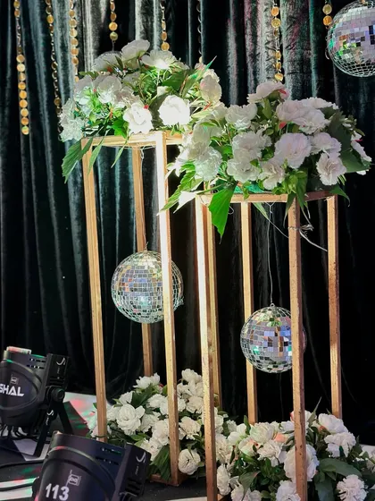 Modern decor elements for a Sangeet, with white flowers and disco balls placed inside tall, golden geometric stands.