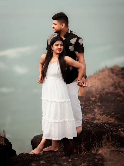 A dramatic pre-wedding portrait of a couple on a clifftop, looking out at the horizon.