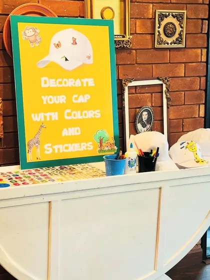 An interactive "Decorate Your Cap" station set up for a jungle-themed party. This station provides white caps, colorful markers, and animal stickers, offering a fun and creative activity for young guests to enjoy and take home a personalized party favor.