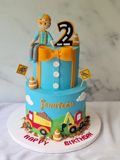 Digging into year two, Blippi style! This two-tier cake is themed around Blippi and construction, with a fondant Blippi figure, edible dirt, and construction vehicles.