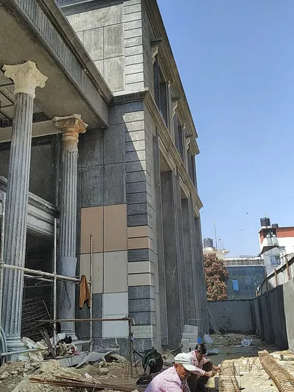 Workers applying stone cladding to the facade of the classical residence, demonstrating the hands-on nature of our site involvement.