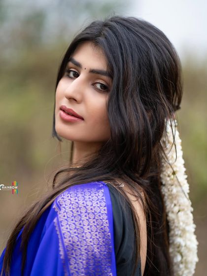 A striking portrait of a model in a royal blue saree, with jasmine flowers in her hair. The close-up shot highlights her expressive eyes and traditional styling.