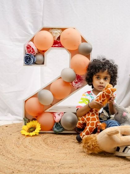 A toddler boy plays with a stuffed giraffe during his second birthday shoot, set against a simple and natural outdoor backdrop.