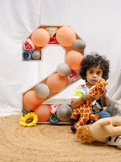 A toddler boy plays with a stuffed giraffe during his second birthday shoot, set against a simple and natural outdoor backdrop.