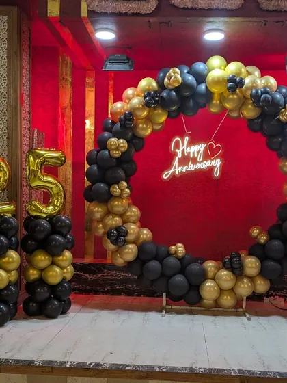 I also create beautiful setups for anniversaries. This 25th-anniversary decoration features a full circular balloon arch in elegant black and gold, a "Happy Anniversary" neon sign, and matching balloon pillars with large foil numbers.