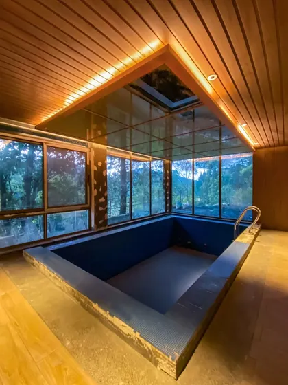 An indoor heated pool designed with a glass ceiling and panoramic windows, blurring the line between the interior and the lush Uttarakhand landscape. This space exemplifies our commitment to luxury design that incorporates natural light and views.