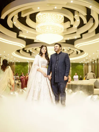A wide shot of the couple standing under a magnificent chandelier, surrounded by smoke, creating a dreamy and grand atmosphere.