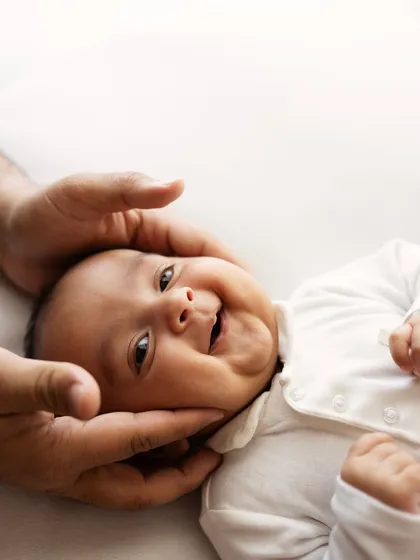 A father's hands gently holding his baby's face, bringing out the most adorable, happy smile.