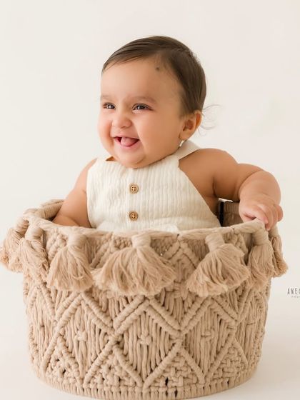 Peeking out with a happy grin. The same baby boy gives a different, adorable expression from his cozy basket during his milestone photoshoot.