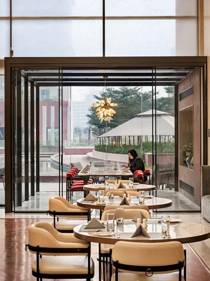 This view from inside the Elevate Clubhouse looks out onto the glass-enclosed dining area and the landscaped terrace beyond. The design maximizes transparency and light, ensuring that even when indoors, residents feel connected to the surrounding environment and the community's social life.