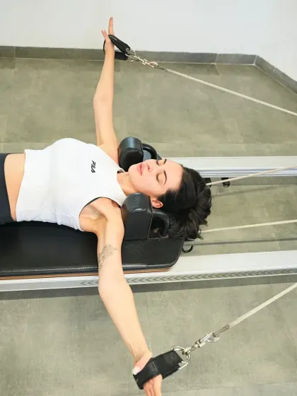 This client enjoys a relaxing and effective stretch on the reformer. The straps provide assistance, allowing her to deepen the stretch and release tension in her shoulders and chest.