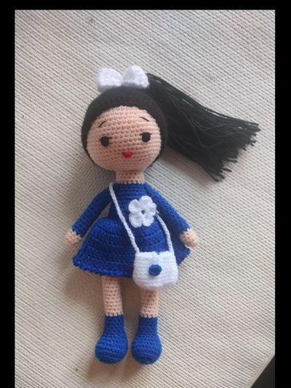 A lovely doll in a blue dress with a white bag and a white flower detail. Her hair is tied back in a high ponytail with a white bow.