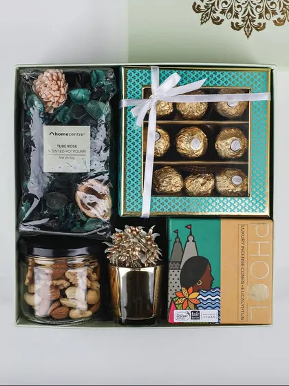 The 'Royal Blend' hamper is a perfect mix of modern and traditional. It features Ferrero Rocher chocolates, a jar of mixed nuts, potpourri, and a decorative golden pineapple.