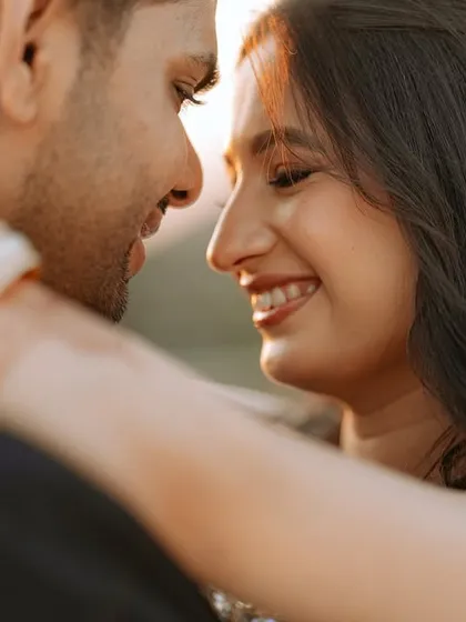 An intimate close-up against the setting sun, focusing on the genuine smiles and connection between the couple.