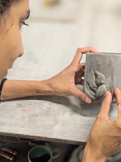 A student carefully adds a textured leaf appliqué to her hand-built mug. This surface decoration technique allows for intricate and personal designs.