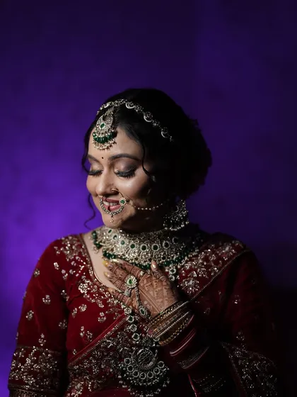 A joyful portrait of the bride, fully ready for her big day. Her smile and the beautiful details of her attire are captured perfectly against a purple backdrop.