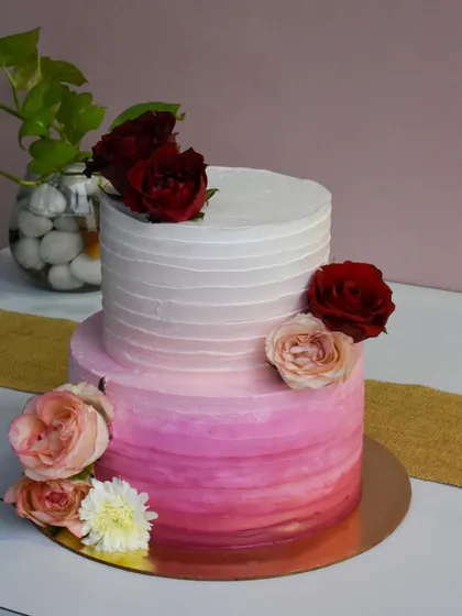 Even a last-minute engagement cake can be a showstopper. This two-tier cake features a beautiful pink ombré effect, fading from a deep rose to a soft white, and is adorned with a mix of fresh flowers.