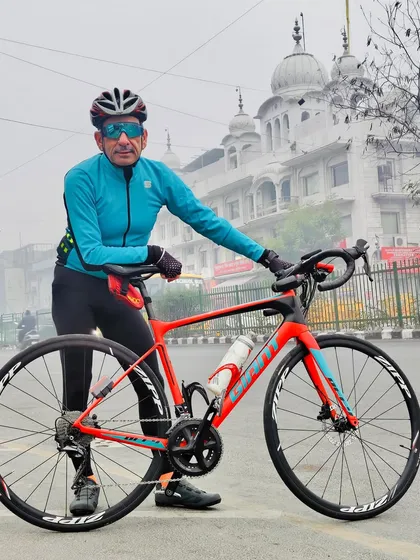 A member with his bright orange Giant Defy bike in front of a Gurudwara, blending cycling with city culture.