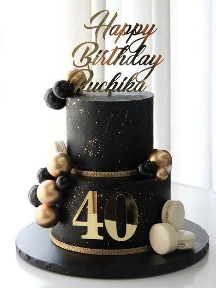 A bold and elegant two-tiered cake for a 40th birthday. The black ganache is accented with gold splatter, chocolate spheres, and macarons for a touch of luxury.
