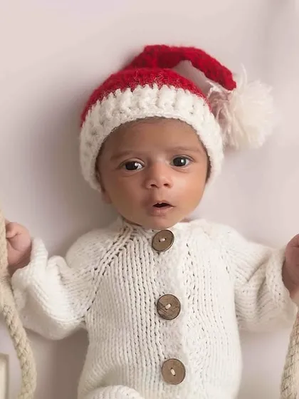 A little Christmas miracle! This newborn is dressed in a cozy Santa hat and knit outfit, ready for his very first holiday season.