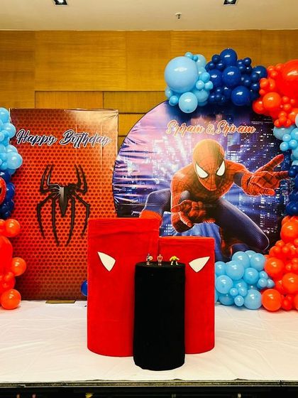 A Spiderman themed stage decoration. This setup includes multiple backdrops with cityscapes and spider logos, and balloon arrangements in the classic red and blue colors.