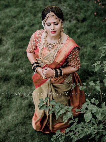 A serene portrait of the bride amidst lush greenery. The traditional makeup, with its defined eyes and rich lip color, stands out beautifully against the natural backdrop.