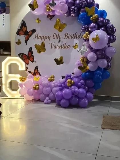 A circular backdrop decorated with purple, blue, and gold balloons for a 6th birthday with a butterfly theme.
