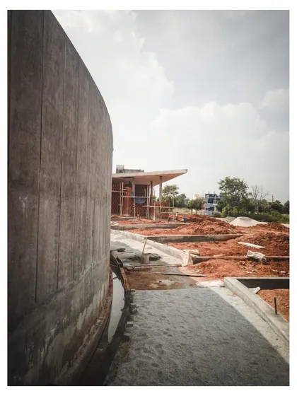 The curved concrete retaining wall of the sunken gallery, with the raw earth of the construction site in the foreground.