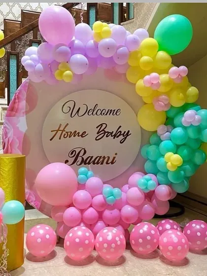 A cheerful 'Welcome Home Baby Baani' decoration. A circular backdrop is surrounded by a colorful pastel balloon garland, creating a sweet and joyful atmosphere.