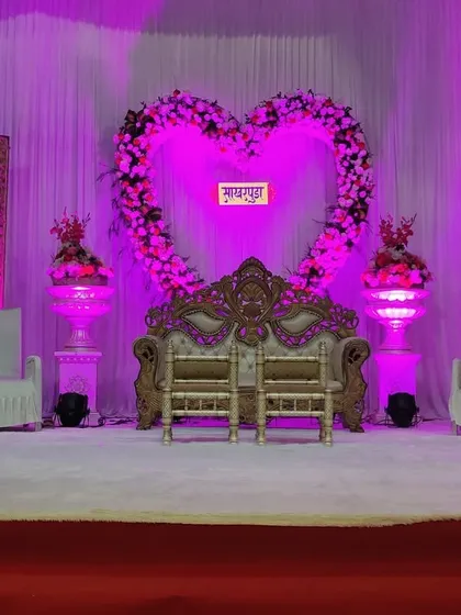 A romantic engagement stage featuring a large heart-shaped floral arch as the centerpiece. The entire setup is bathed in a soft purple light, creating a dreamy atmosphere for the couple's special moment.