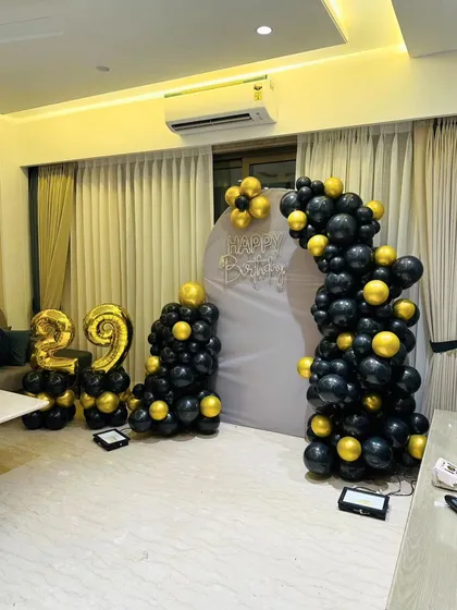A classic black and gold 29th birthday setup with a fabric backdrop and balloon arch.