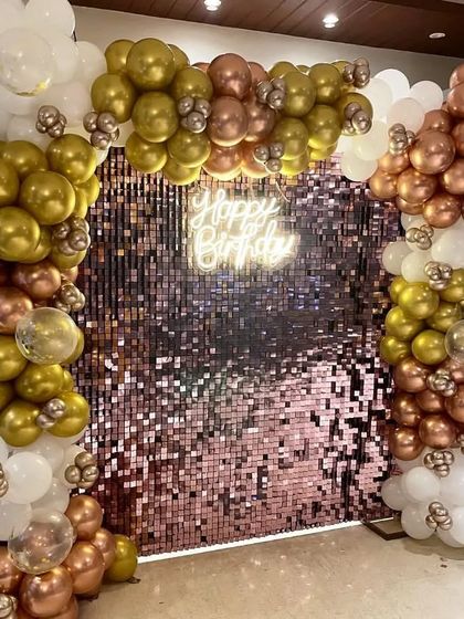 This angle highlights the shimmer of the rose gold sequin wall. I use high-quality sequin panels to ensure the backdrop sparkles and looks great in photos. The balloon colors, like the gold and white seen here, can be customized to match your party's theme.