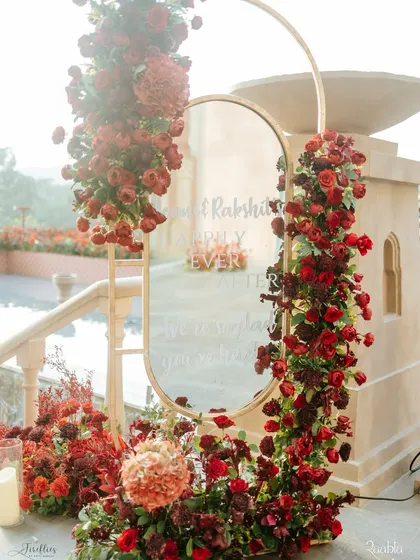 A beautiful welcome sign for the 'Laal Ishq' wedding. The message is written on a mirror, which is elegantly framed with an abundance of red roses and hydrangeas.