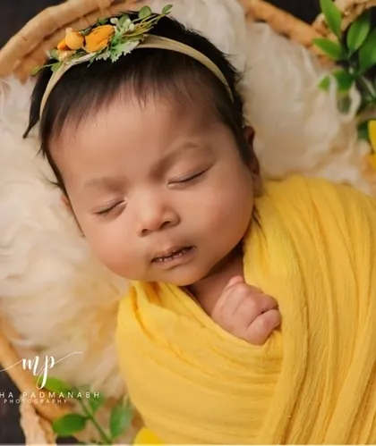 A close-up portrait of the baby in the basket, focusing on their sweet, sleeping face and the delicate floral headband.