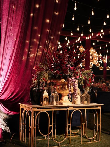 An elegant console table at the entrance, styled with rich florals, lanterns, and dramatic burgundy drapes. The string lights in the background created a magical, starry-night effect over the entire venue.