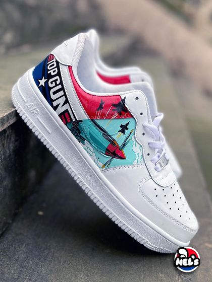 A stylish shot of the 'Top Gun' custom Nike AF1, showing the full side profile with the jet artwork and movie logo against a concrete background.