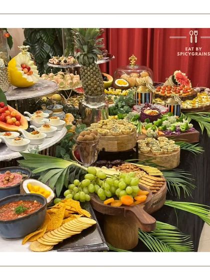 A beautiful grazing table featuring a mix of savoury and sweet items, including tacos, fruit tarts, and fresh fruit, all arranged with care and artistry.