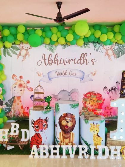 A vibrant jungle theme for a "Wild One" first birthday. This setup is packed with details, including a full balloon arch in shades of green, animal cutouts, themed plinths, and a large light-up number '1'.