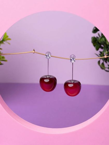 A creative shot of cherry-shaped earrings hanging from a branch inside a circular frame. We love experimenting with props and compositions to create unique jewellery photos.