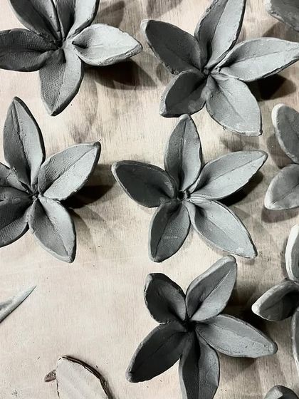 A collection of clay blossoms, each petal individually shaped by hand. These will later be assembled into larger sculptural works or used as decorative elements.