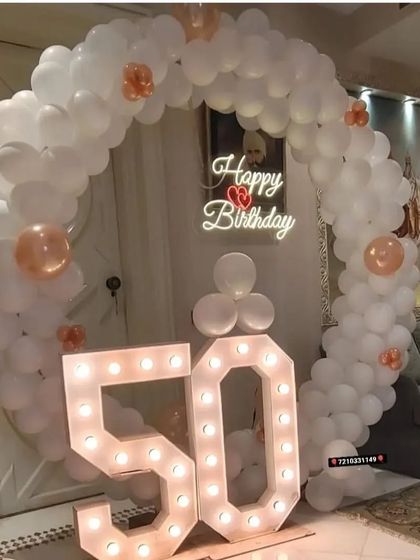 A 50th birthday party with a white balloon ring, a neon sign, and large "50" marquee numbers.