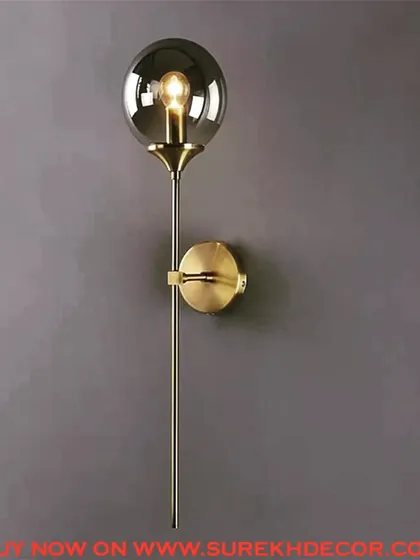 A sophisticated wall lamp with a smoked glass globe on a long, slender rod. The antique brass finish adds a touch of vintage elegance to this modern and minimalist design.