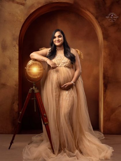 A regal portrait of an expecting mother in a golden gown, posing with a vintage globe to symbolize the world she's bringing a new life into.