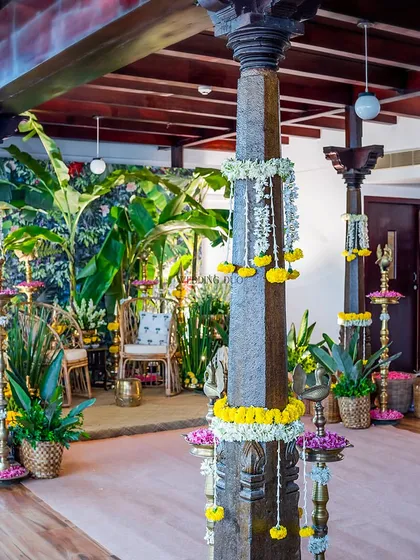 A serene blend of heritage and freshness. This Haldi setup features traditional pillars decorated with flowers, surrounded by banana plants and woven details for a cozy and modern-traditional vibe.