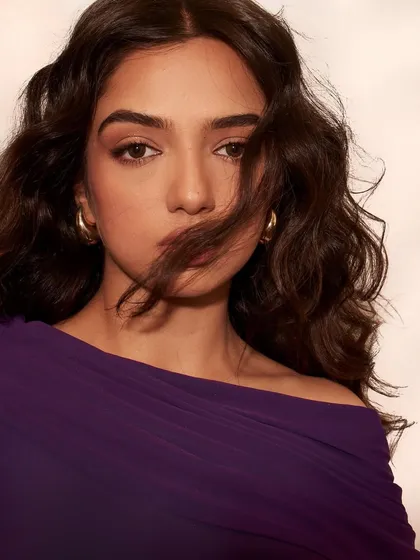 A close up portrait of Ahsaas Channa for her Elle feature. The soft, windswept hair and simple gold hoops complement the rich purple of the dress without overpowering it.