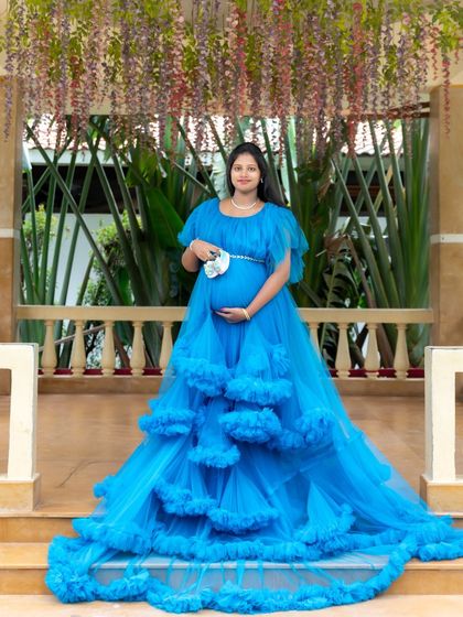A beautiful portrait of a mom-to-be in a blue ruffled gown, holding a small pair of baby shoes on a veranda.
