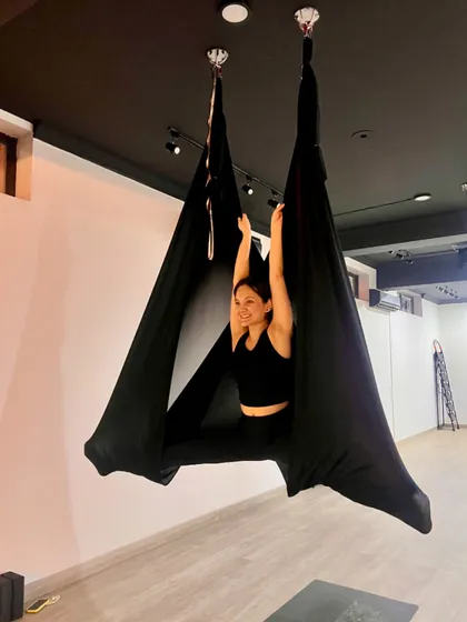 Move to feel alive. A student enjoys a wide-legged split inside the cocoon of the hammock, smiling and embracing the moment.