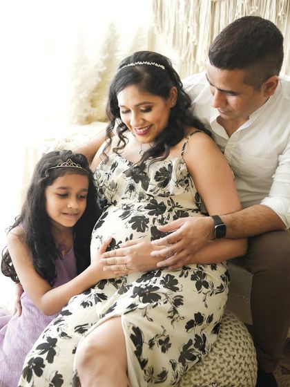 This shot shows a complete family maternity session, with the older sister sharing her excitement. The bright, natural light from the window creates a soft and gentle mood.