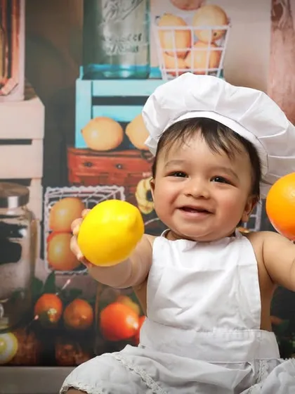 This happy little chef is showing off his favorite ingredients, a lemon and an orange. The fruit and kitchen-themed backdrop adds a colorful and playful element to this first birthday session.