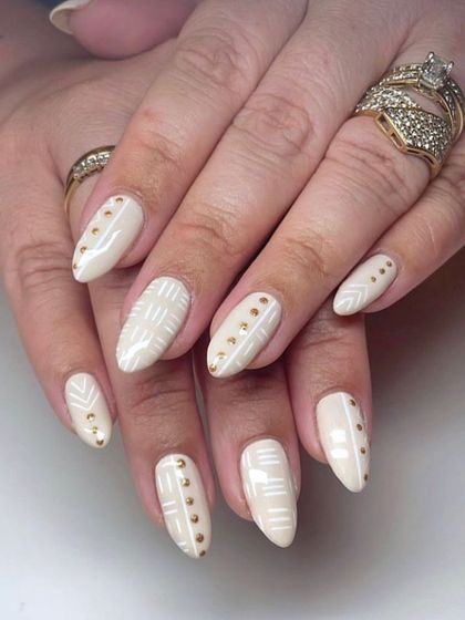 A chic, bohemian-inspired design with off-white nails, detailed with fine white lines and gold stud accents.